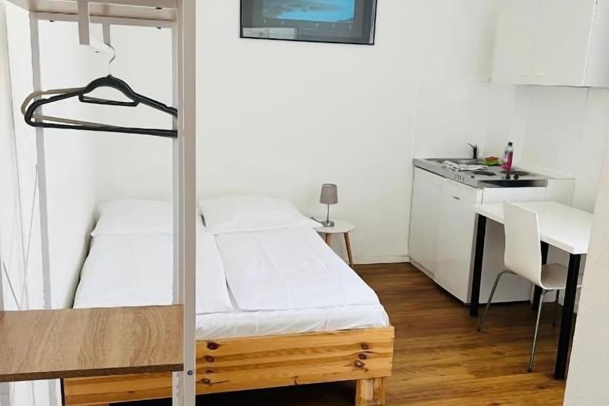 A room with a bunk bed, a desk, a chair, a small table, and a picture on the wall.