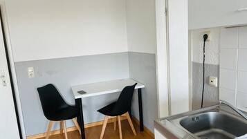 Eine kleine Küche mit weißer Arbeitsplatte, zwei schwarzen Stühlen, einer Edelstahl-Spüle und Holzboden.