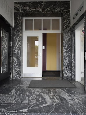 Un área de recepción con suelo de mármol, puerta de cristal y mostrador de recepción.