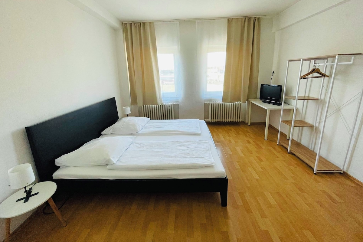 A hotel room with a bed, a desk with a television, a wardrobe, and a radiator.