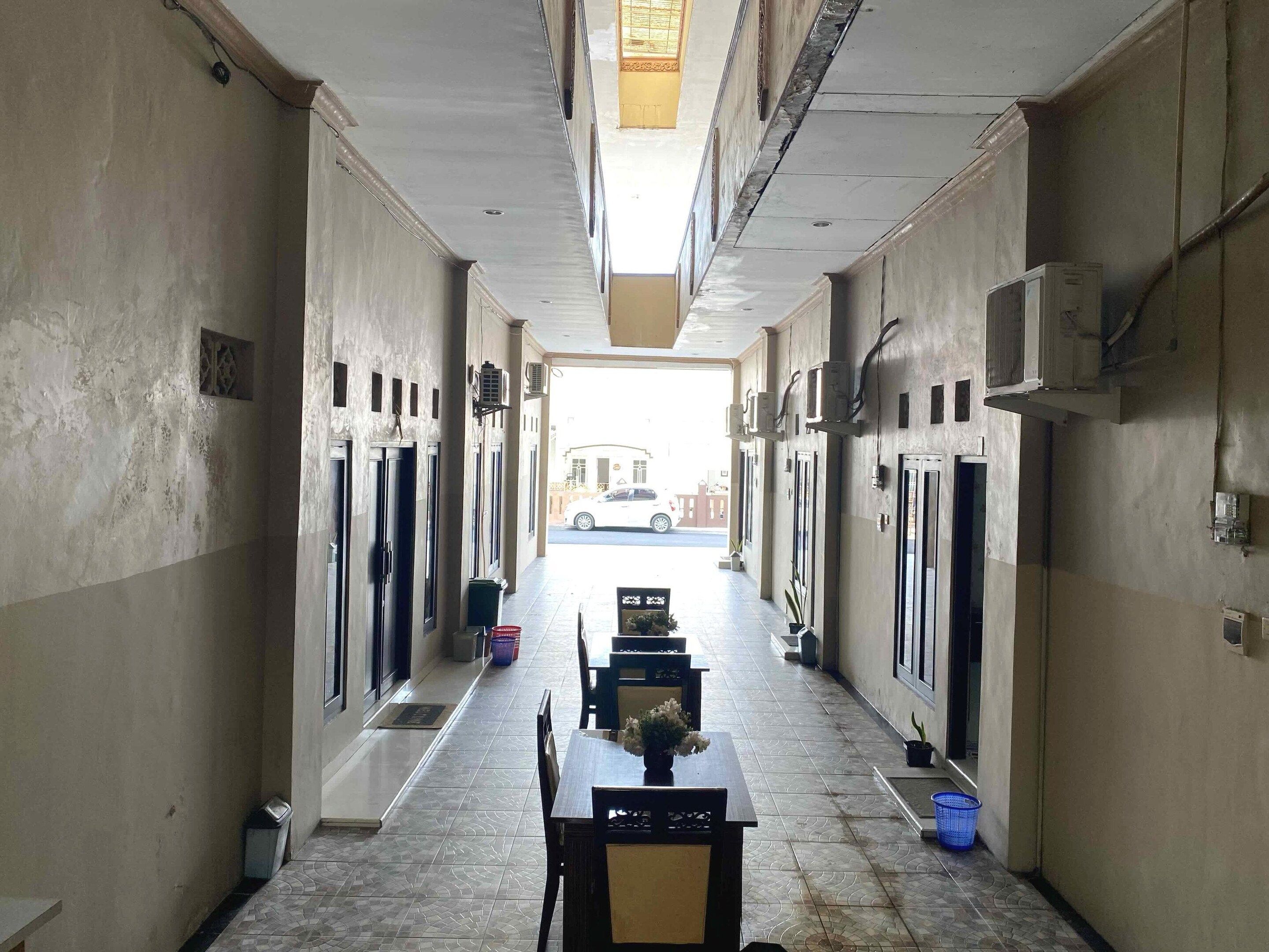 A corridor with doors on both sides, a tiled floor, and a table with chairs in the center.
