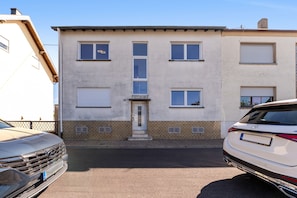 A building with a central entrance, multiple windows, and a garage area with parked cars. - Apartment "Onjito" with Shared Garden, Balcony, and Wi-Fi (Saarbrücken)