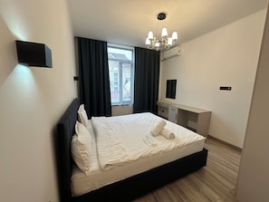 A hotel room with a bed, a desk, a chair, a window with curtains, and a ceiling light fixture.