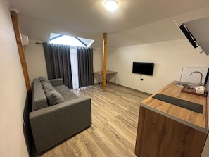 A modern living space with a sofa, a small table, a TV, and a wooden counter with a sink.