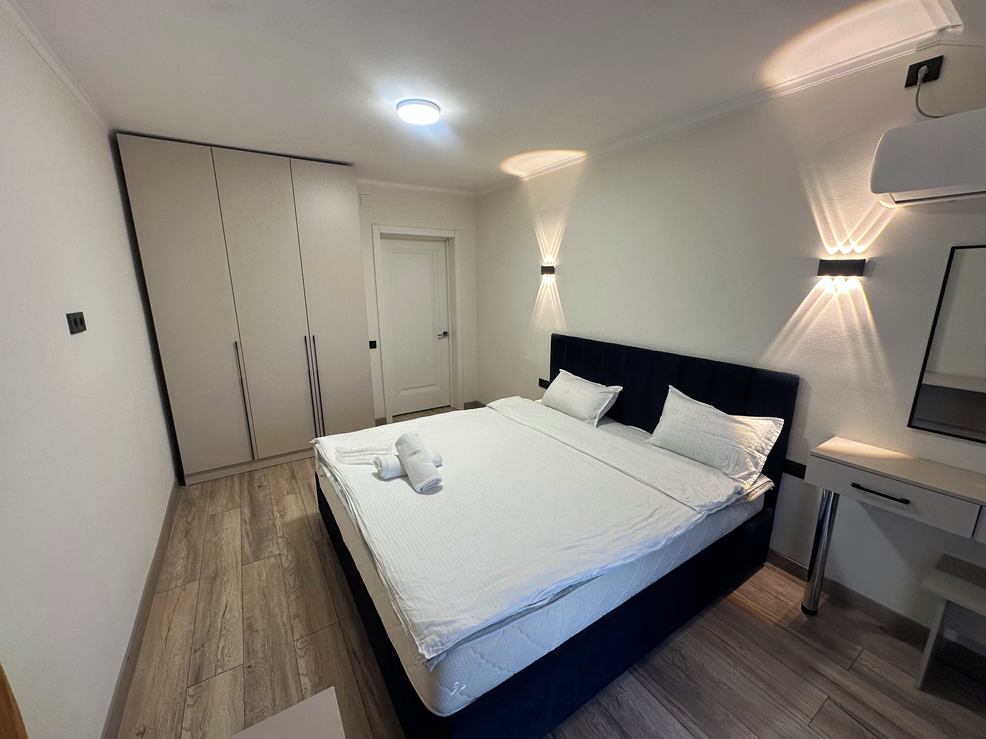 Une chambre à coucher comprenant un lit, des tables de chevet, une armoire et un luminaire fixé au mur.