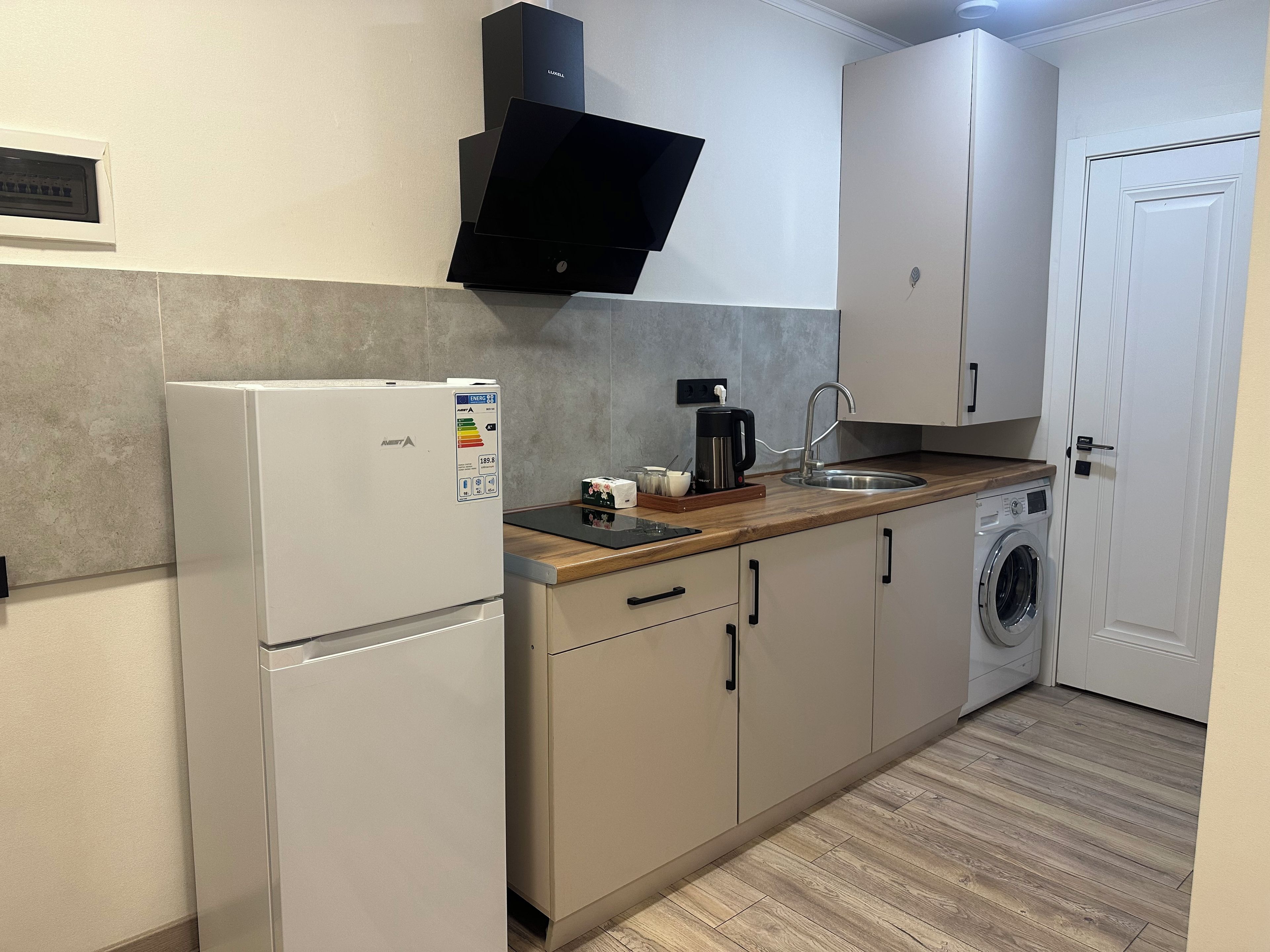 Cocina compacta con refrigerador, cafetera, lavadora y pileta.