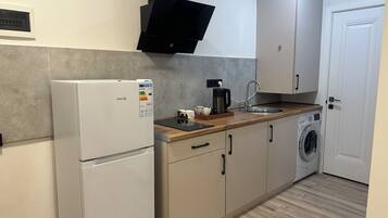 Cocina compacta con refrigerador, cafetera, lavadora y pileta.