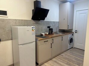 A compact kitchen with a refrigerator, a coffee maker, a washing machine, and a sink.