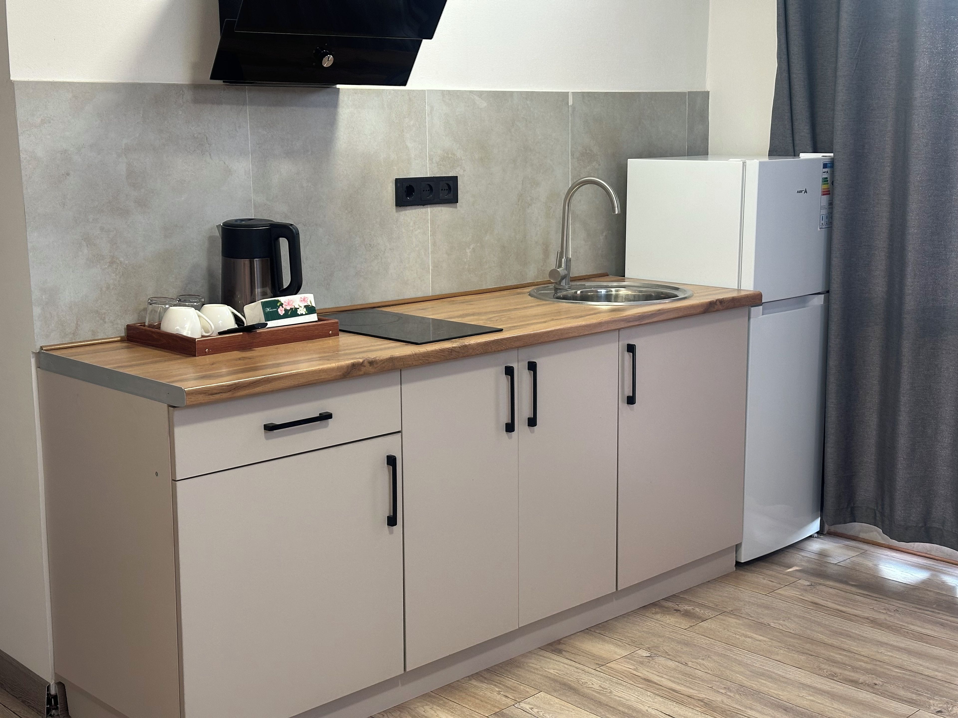 Une cuisine compacte avec un plan de travail en bois, une machine à café, un évier et un réfrigérateur blanc.