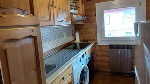 Cozinha de cabana de madeira com máquina de lavar, fogão e janela com vista.