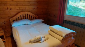 Una habitación de cabaña de madera con cama, almohadas y una ventana con cortinas.