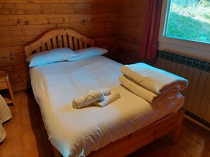 A wooden cabin room with a bed, pillows, and a window with curtains. - Three-Room Apartment in Mountain Cabin Style (Vezza d'Oglio)