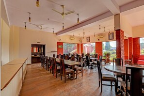 A spacious dining area with multiple tables and chairs, a washroom sign, and a view of the outdoors through large windows.