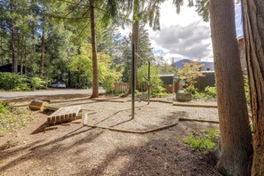 Ein von Bäumen umgebener Campingplatz mit Kiesflächen, Holzbänken und einer Metallkonstruktion.