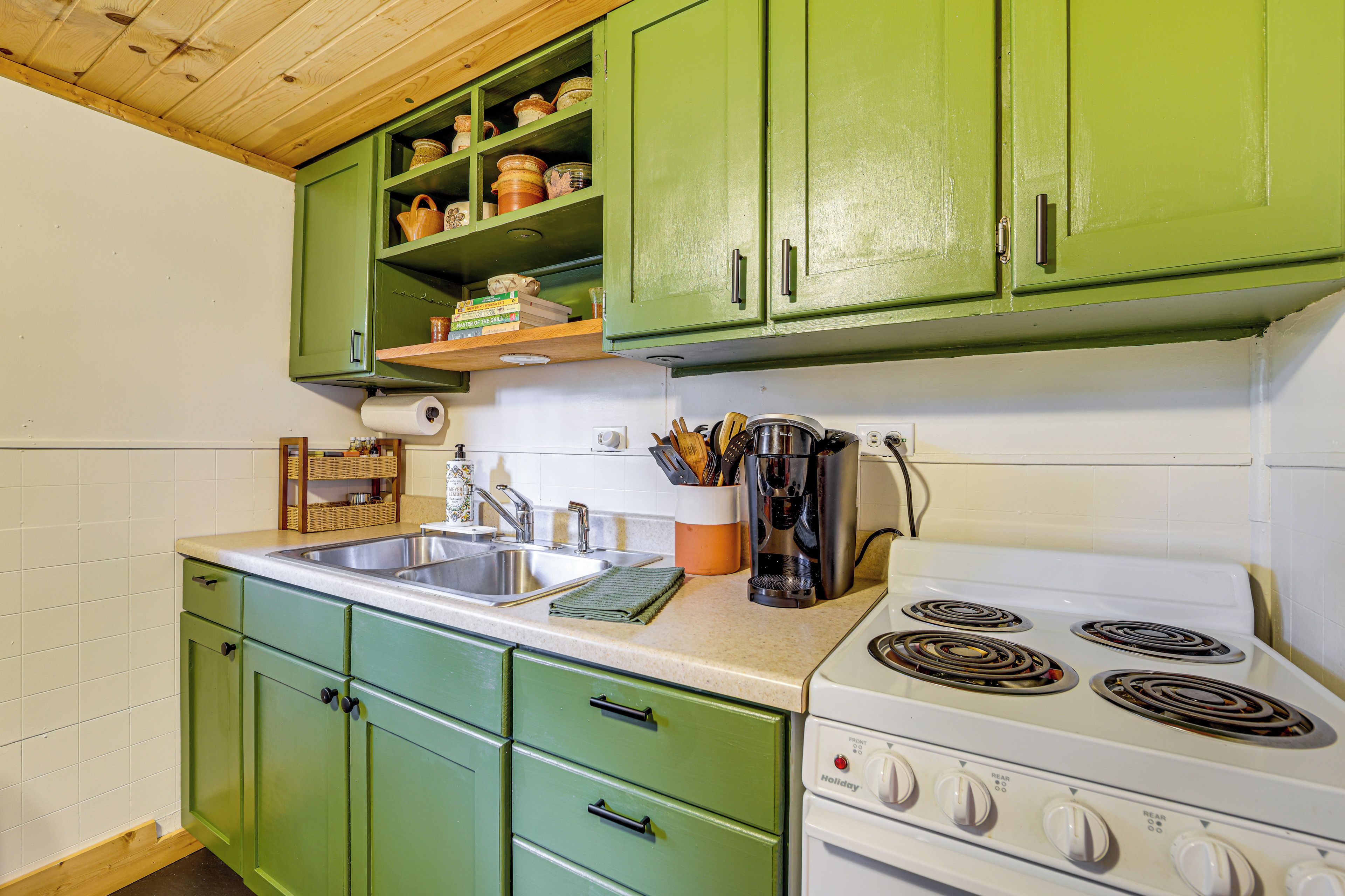 A kitchen with green cabinets, a white stove, and a sink.