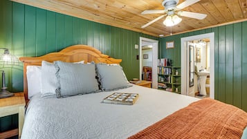 Una camera da letto con una testiera in legno, un letto con copriletto e cuscini, una ventola a soffitto, un comodino con una lampada e una libreria.