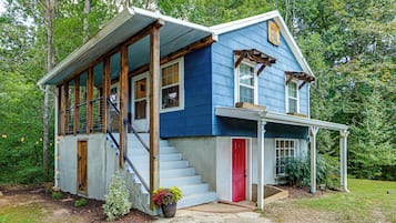 A two-story house with a porch, wooden staircase, and a red door.