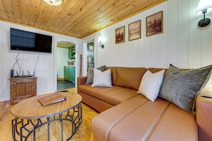 A cozy living room with a brown leather sofa, a wooden coffee table, and a flat-screen TV mounted on the wall. - Cozy Candler Cottage, Near Hiking and Wildlife (Candler)