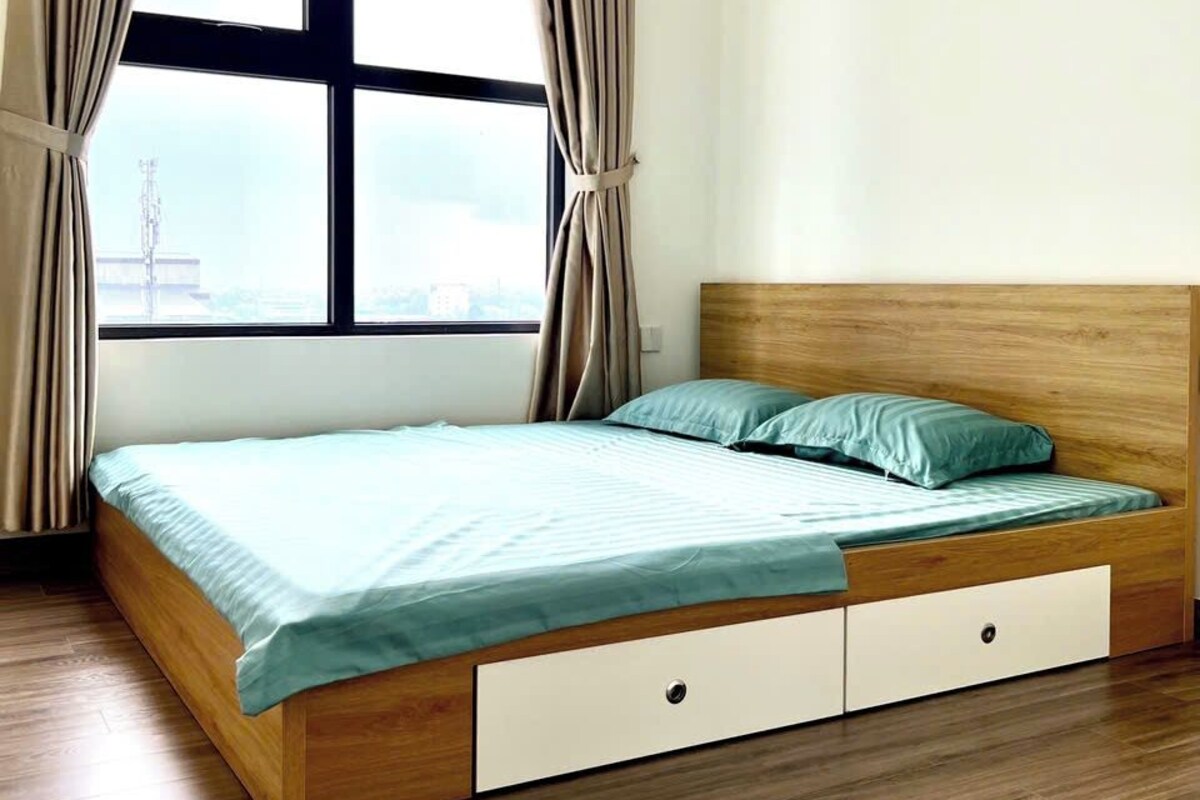 Quarto com cama de madeira, janela com cortinas e vista para a paisagem urbana.
