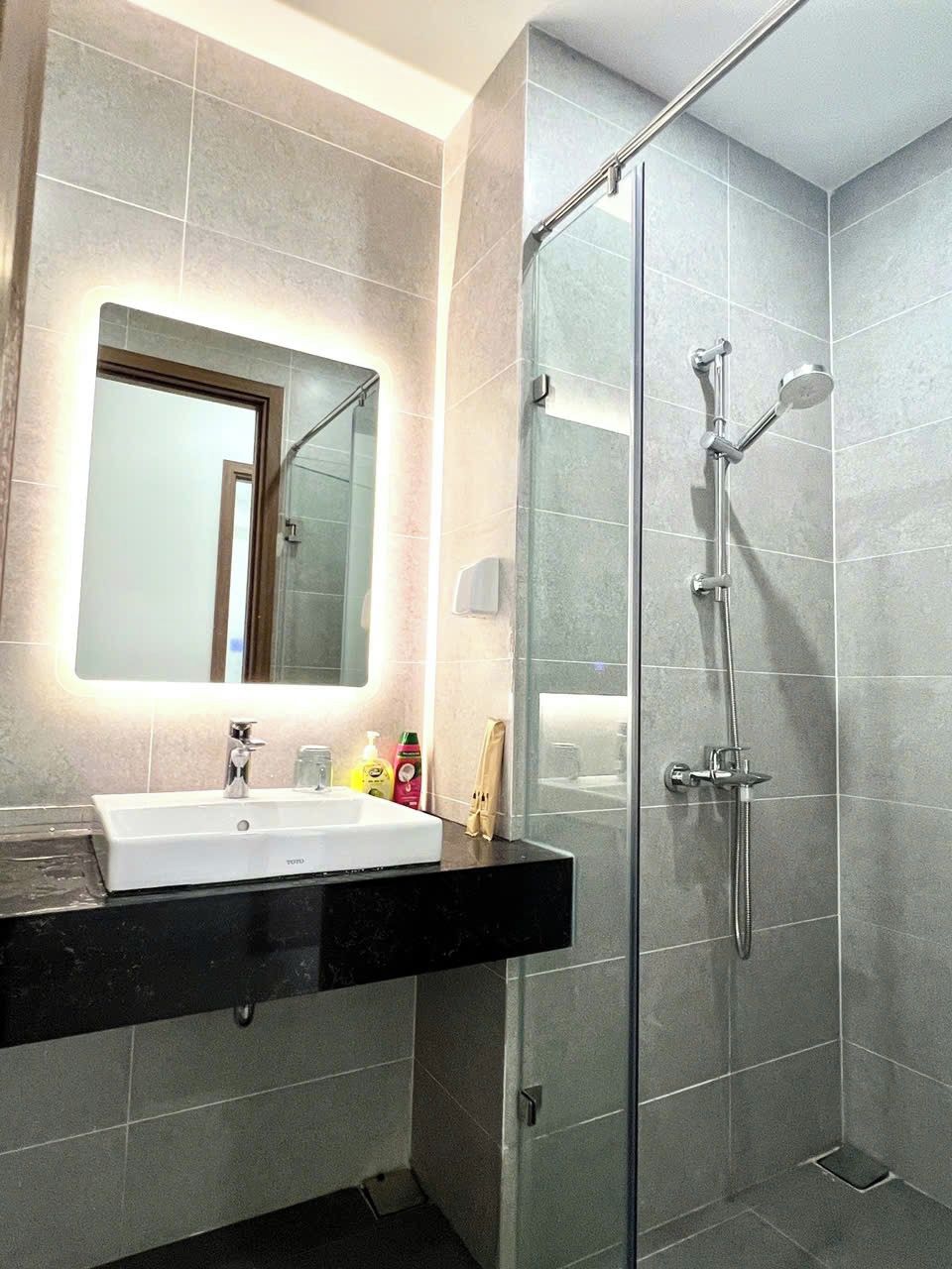 Ein modernes Badezimmer mit einer Duschkabine aus Glas, einem Waschbecken inklusive Spiegel und Toilettenartikeln auf der Ablagefläche.