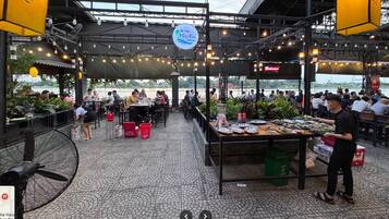 An outdoor dining area with tables and chairs, a vendor stand, and a view of a body of water.