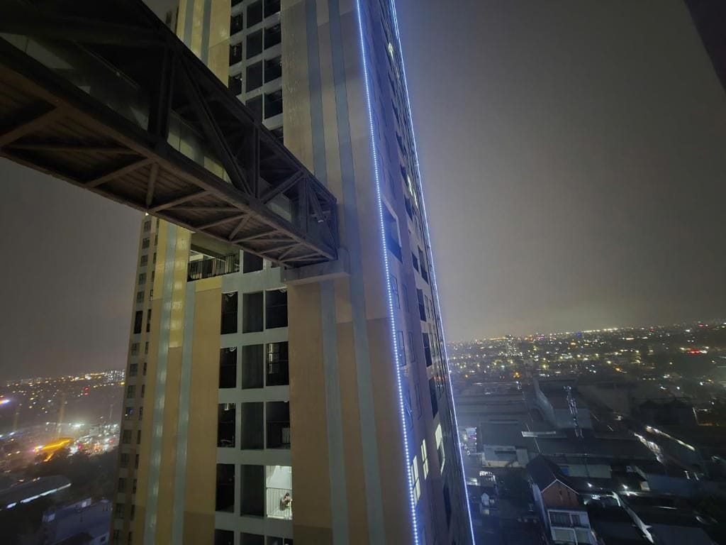 Ein Hochhaus mit einer markanten, blau beleuchteten Fassade und sichtbarer Brückenkonstruktion.