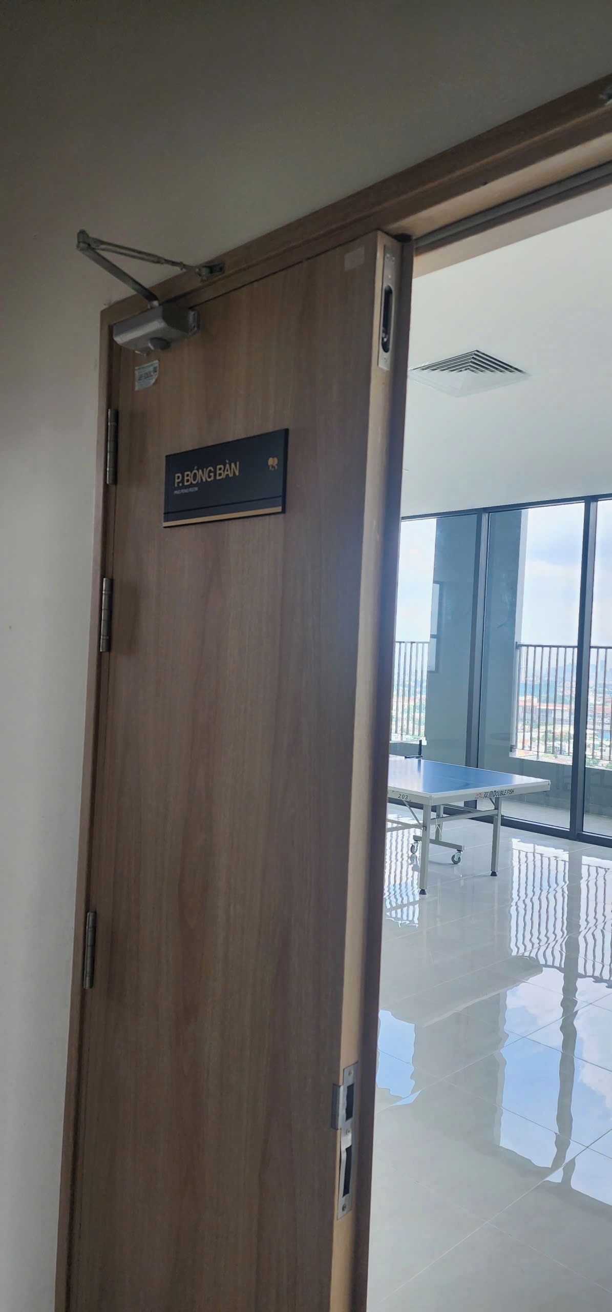 Una puerta de madera con una placa que dice 'P. BÓNG BÂN' y vistas a un balcón con una mesa y sillas.