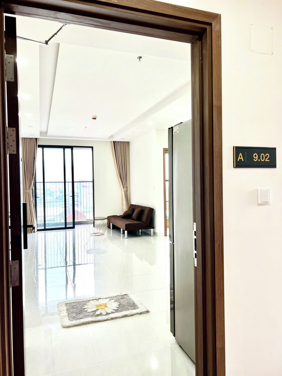 Quarto de hotel moderno com uma grande porta de vidro deslizante que dá para uma varanda, um sofá e um tapete pequeno.
