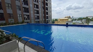 Piscina com escada de metal, rodeada por um edifício com várias varandas.