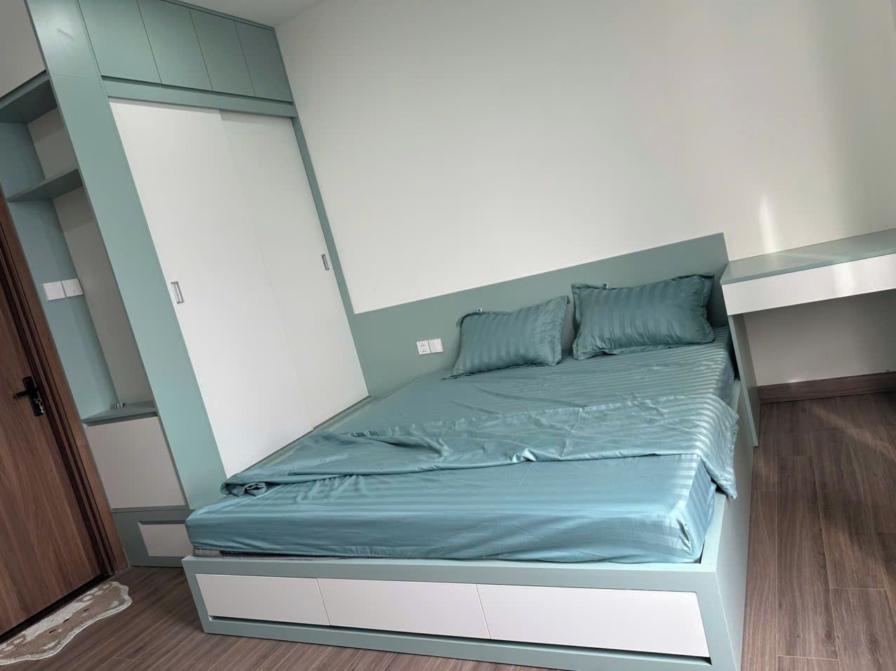 Une chambre individuelle avec un lit simple, une armoire intégrée, une porte et un plancher en bois.