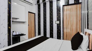 Habitación de hotel con cama, mesita de noche con hervidor y armario con espejo.