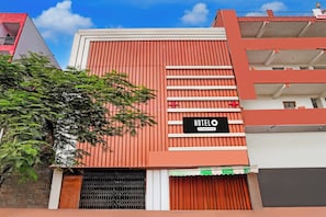 A hotel with a red facade, a sign indicating it is company-serviced, and a visible window. - Hotel O Sector 121 Gaur City Mall Noida (Noida)