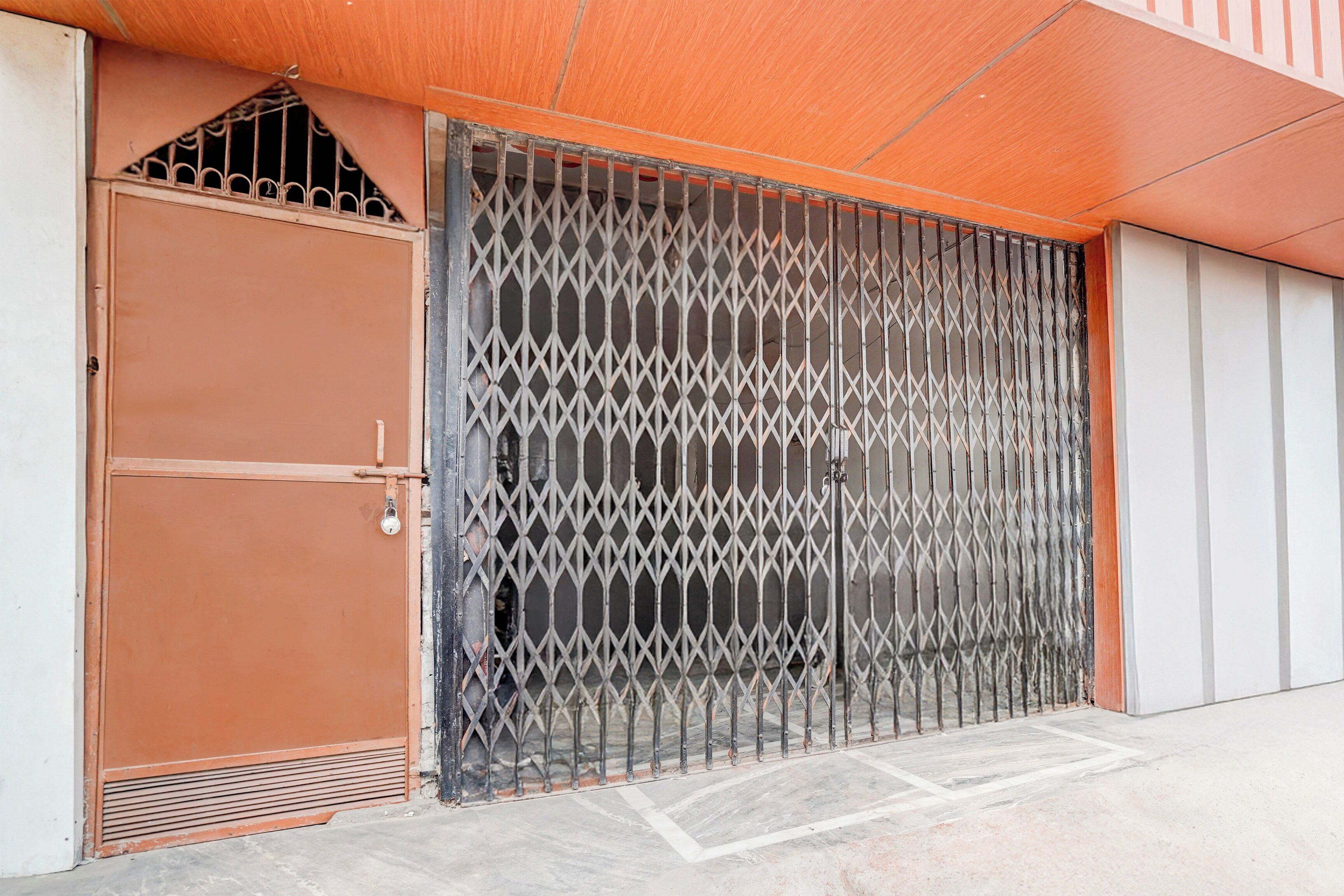 A metal gate with a diamond-patterned design, a brown door with a lock, and a tiled floor.