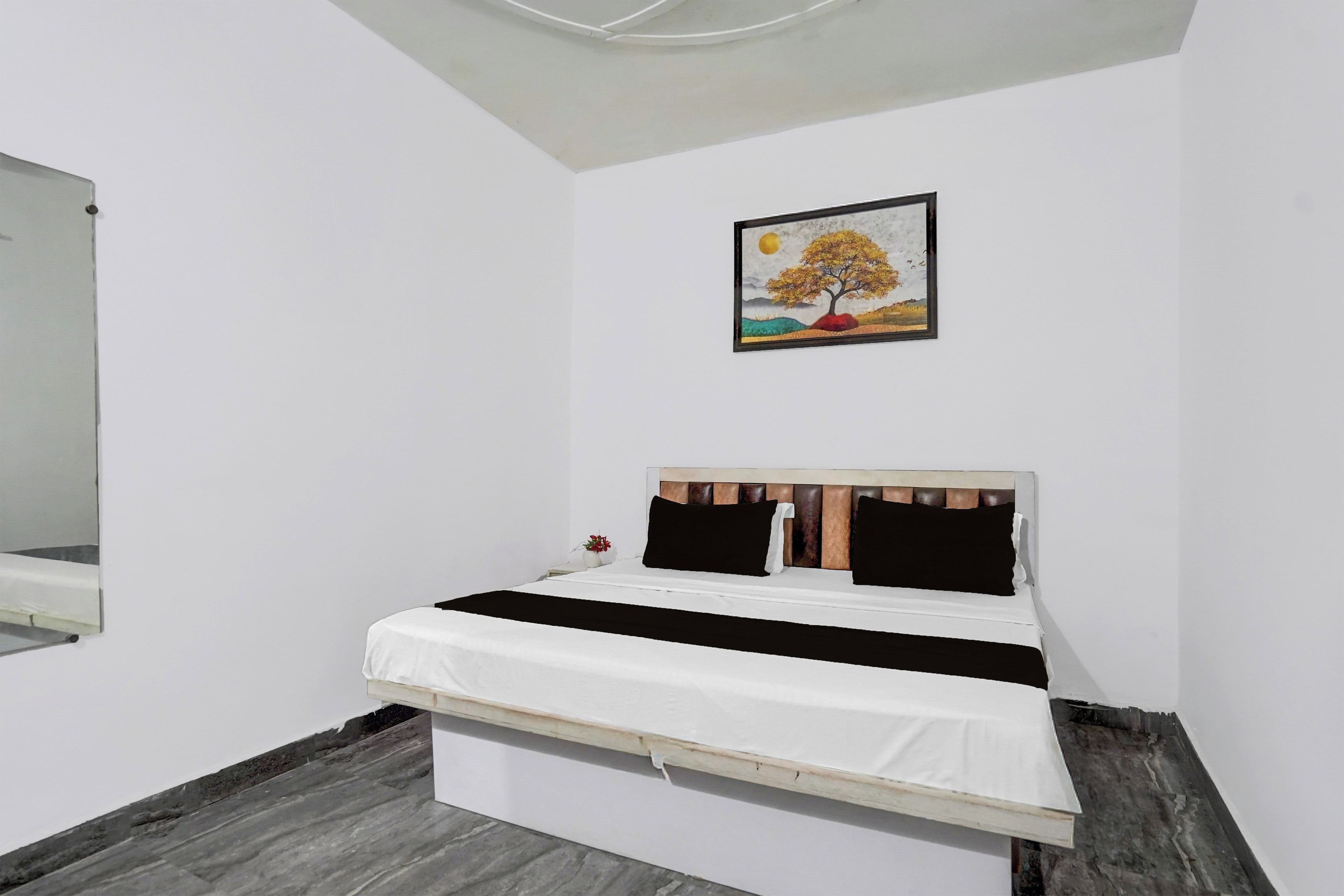 Una cama individual con cabecera de madera, ropa de cama blanca y un cuadro de un árbol en la pared.