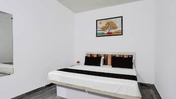 Una cama individual con cabecera de madera, ropa de cama blanca y un cuadro de un árbol en la pared.