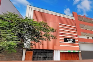 A hotel with a red facade, a signboard, and a tree in front.