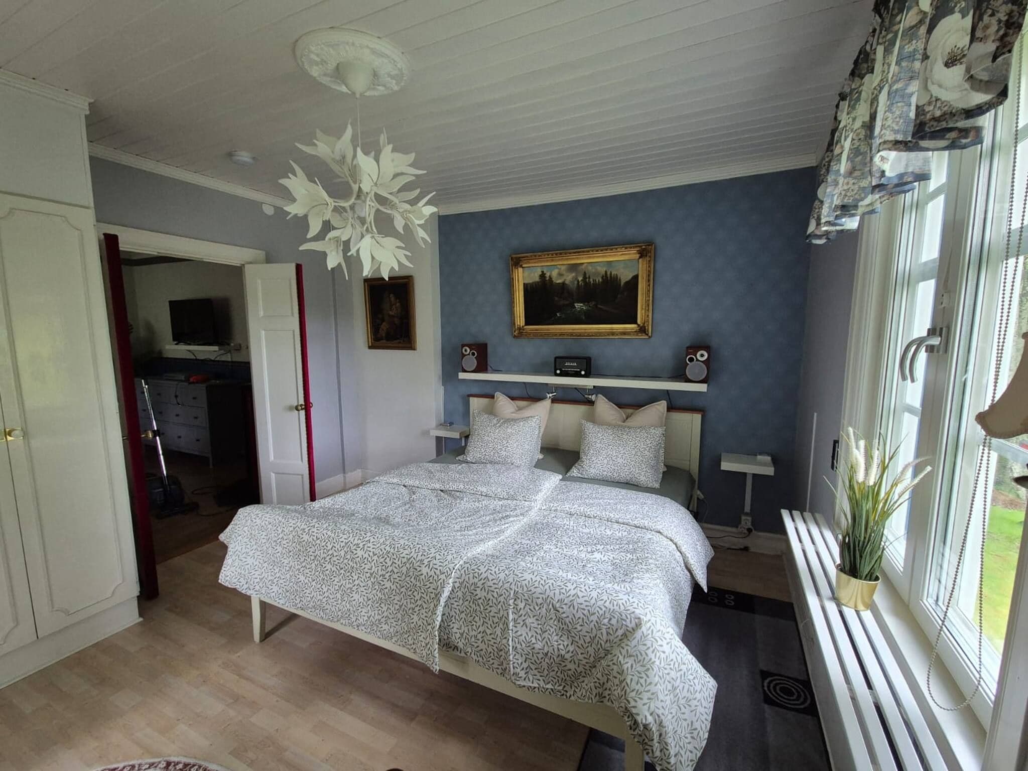 A bedroom with a bed, a painting, a window with curtains, and a ceiling fan.