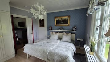 A bedroom with a bed, a painting, a window with curtains, and a ceiling fan.