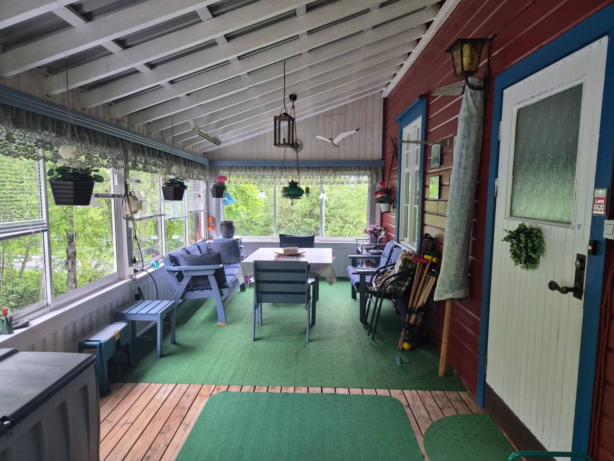 A covered patio with a green artificial turf floor, a wooden deck, and a seating area with a table and chairs.