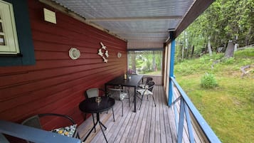 A covered wooden deck with a red wall, a table with chairs, and a view of the surrounding greenery.