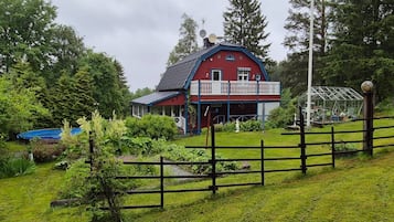 A red barn with a balcony, surrounded by lush greenery and a wooden fence.
