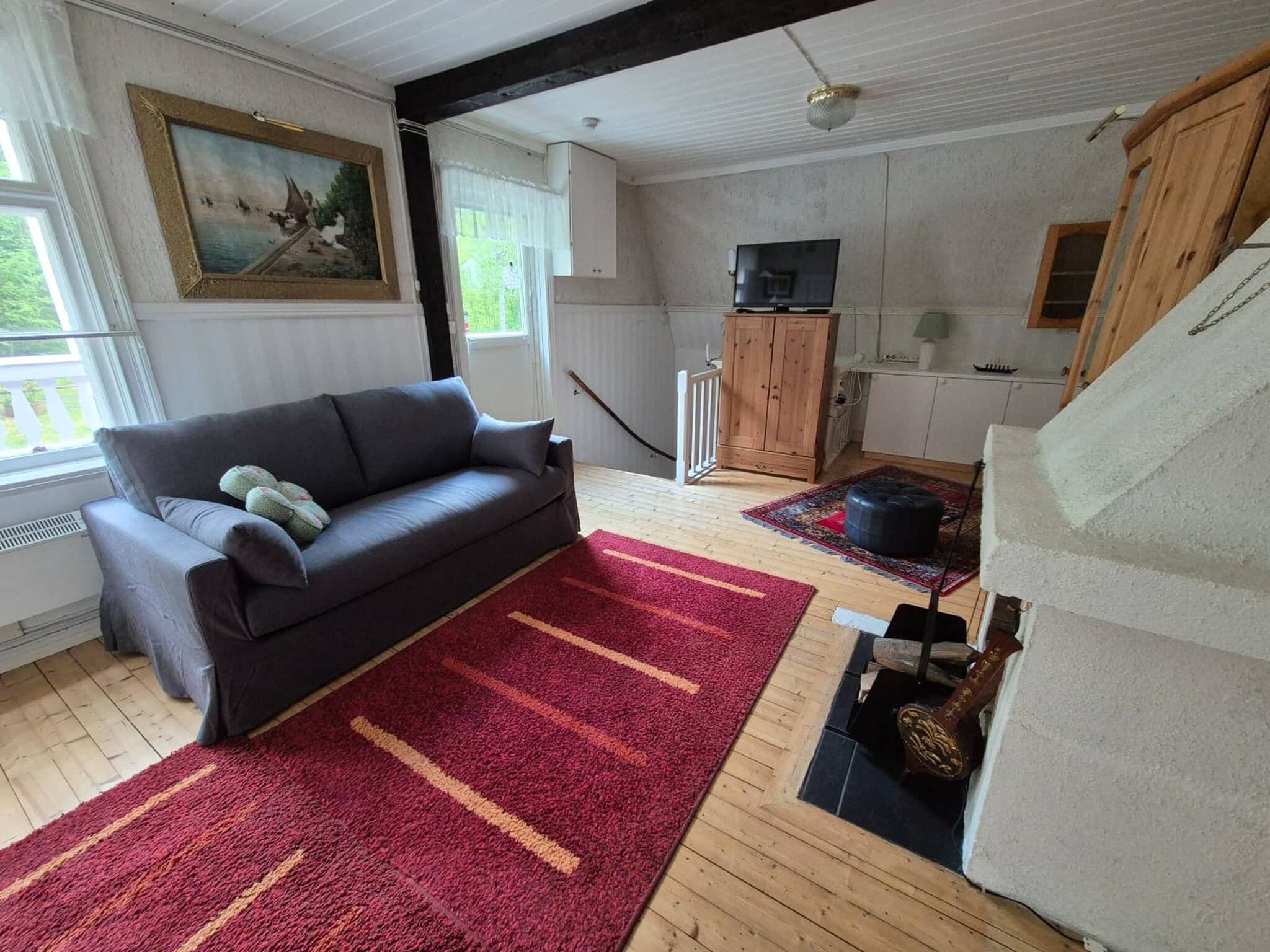 A living room with a sofa, a red rug, a wooden cabinet, and a television.