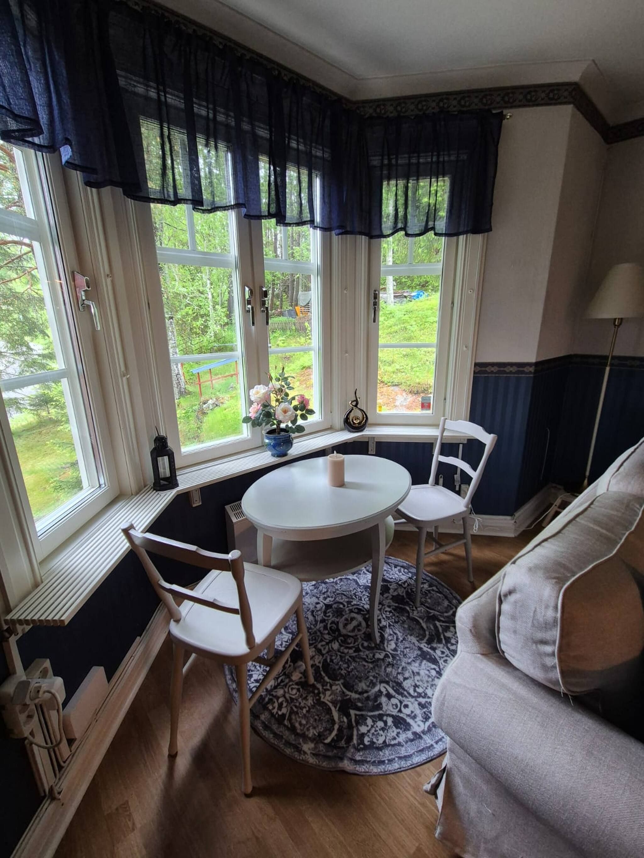 A room with a bay window, a round table with chairs, a patterned rug, and a sofa.
