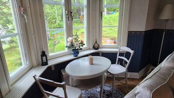 A room with a bay window, a round table with chairs, a patterned rug, and a sofa.