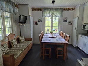 A cozy room with a wooden sofa, a dining table with chairs, a television on a stand, and a kitchen area with a microwave.