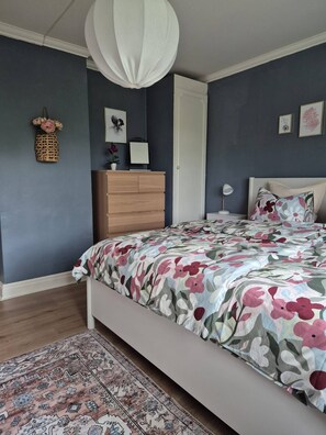 Un dormitorio con cama, mesita de noche, lámpara y estante en la pared con adornos.