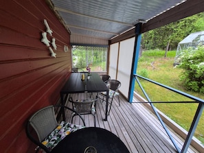 An outdoor patio with a table and chairs, a covered area with a view of greenery, and a glass greenhouse structure. - Holiday House With Lots of Charm (Lunde)