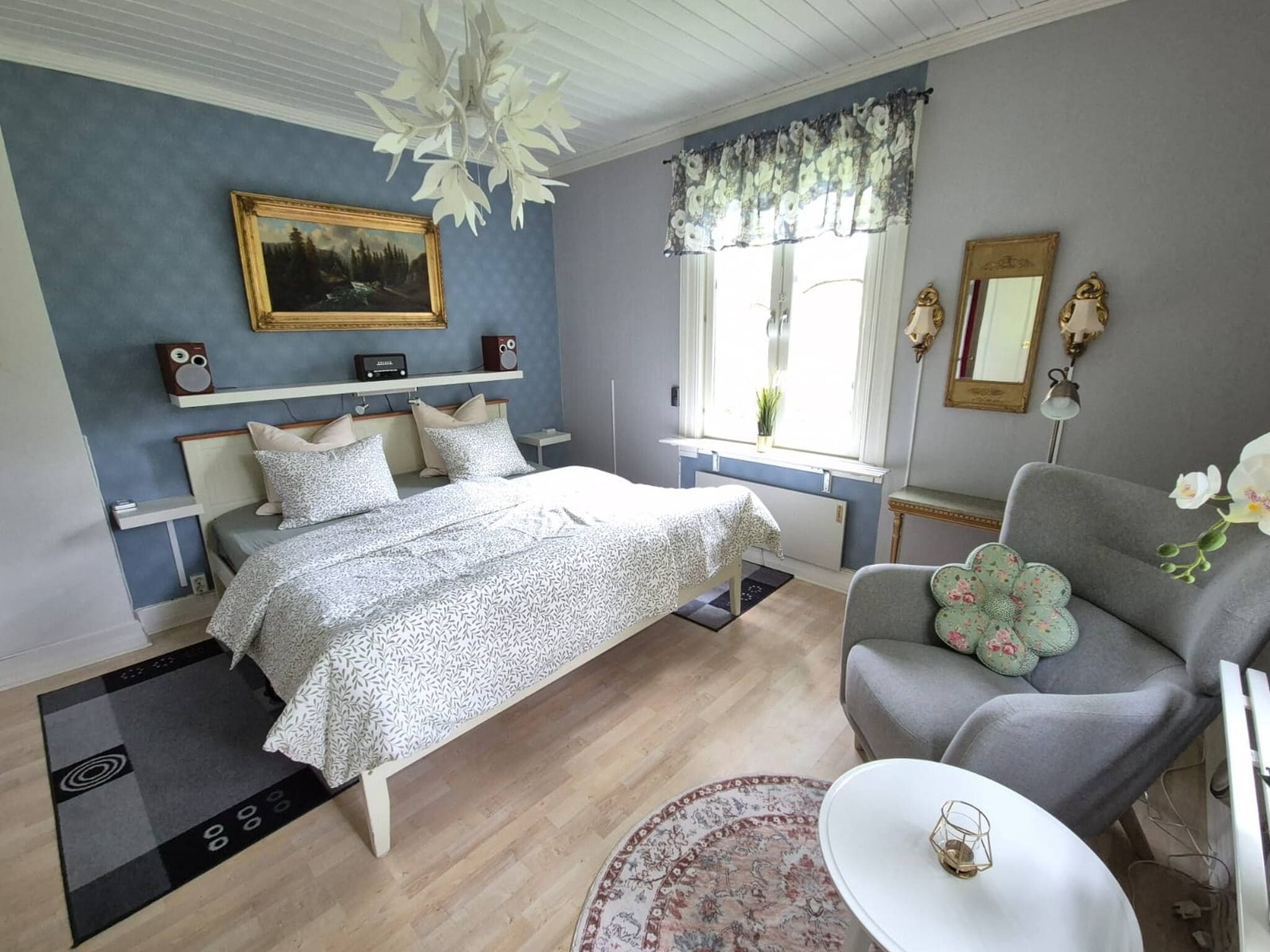 A bedroom with a bed, bedside tables, a chair, a small table, a mirror, and a window with curtains.