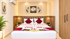 Een hotelkamer met een groot bed, een plafondventilator, wandairconditioning en bloemkunstwerken in lijsten.