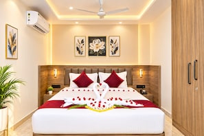 Habitación de hotel con una cama grande, ventilador de techo, aire acondicionado instalado en la pared y una obra de arte floral enmarco.